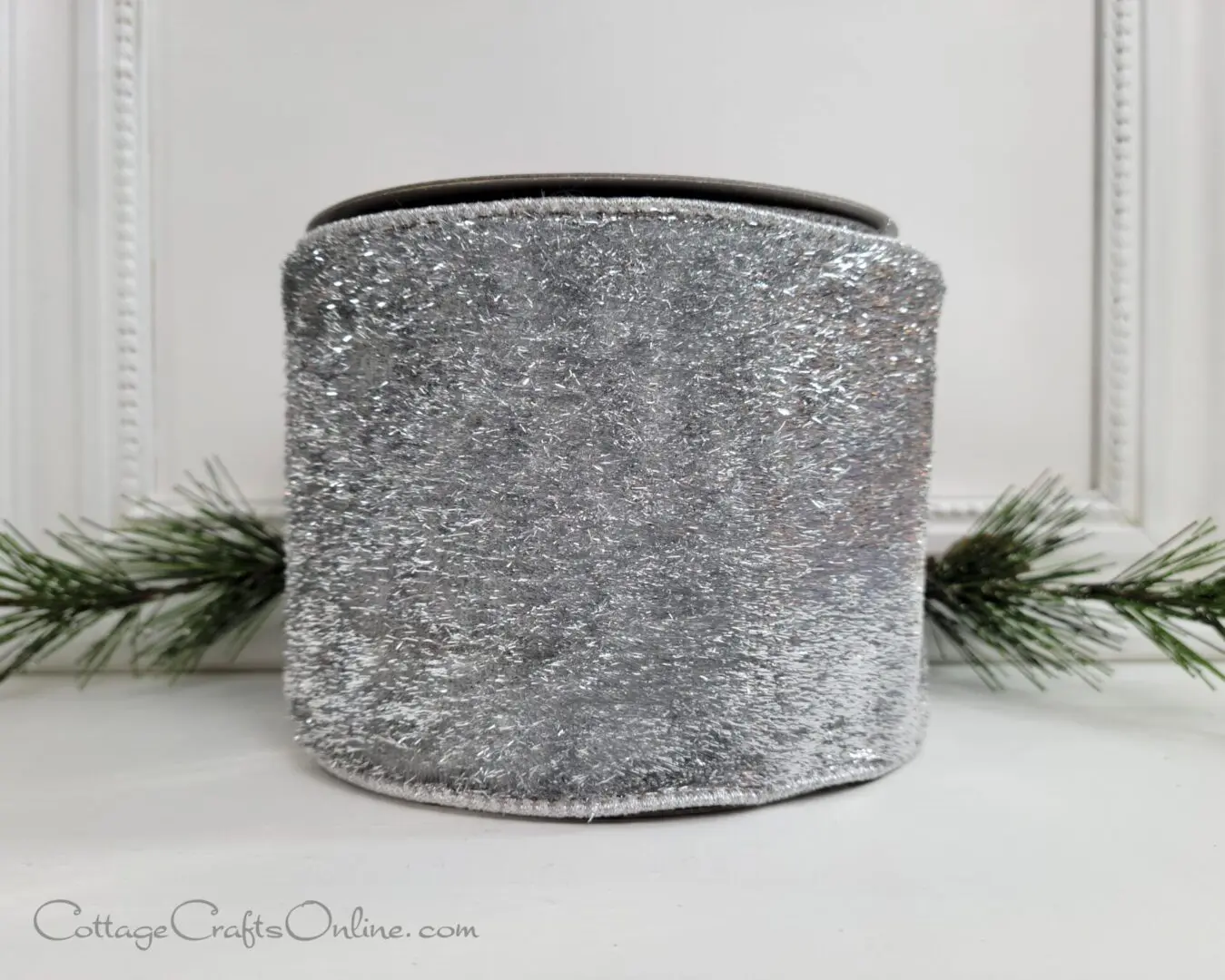 a silver sequin candle holder adorned with t2022 new holiday ribbons, sitting on a mantle.