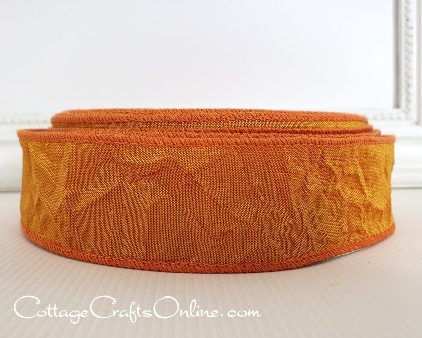 A roll of orange ribbon from Cottage Crafts Online on a white table.