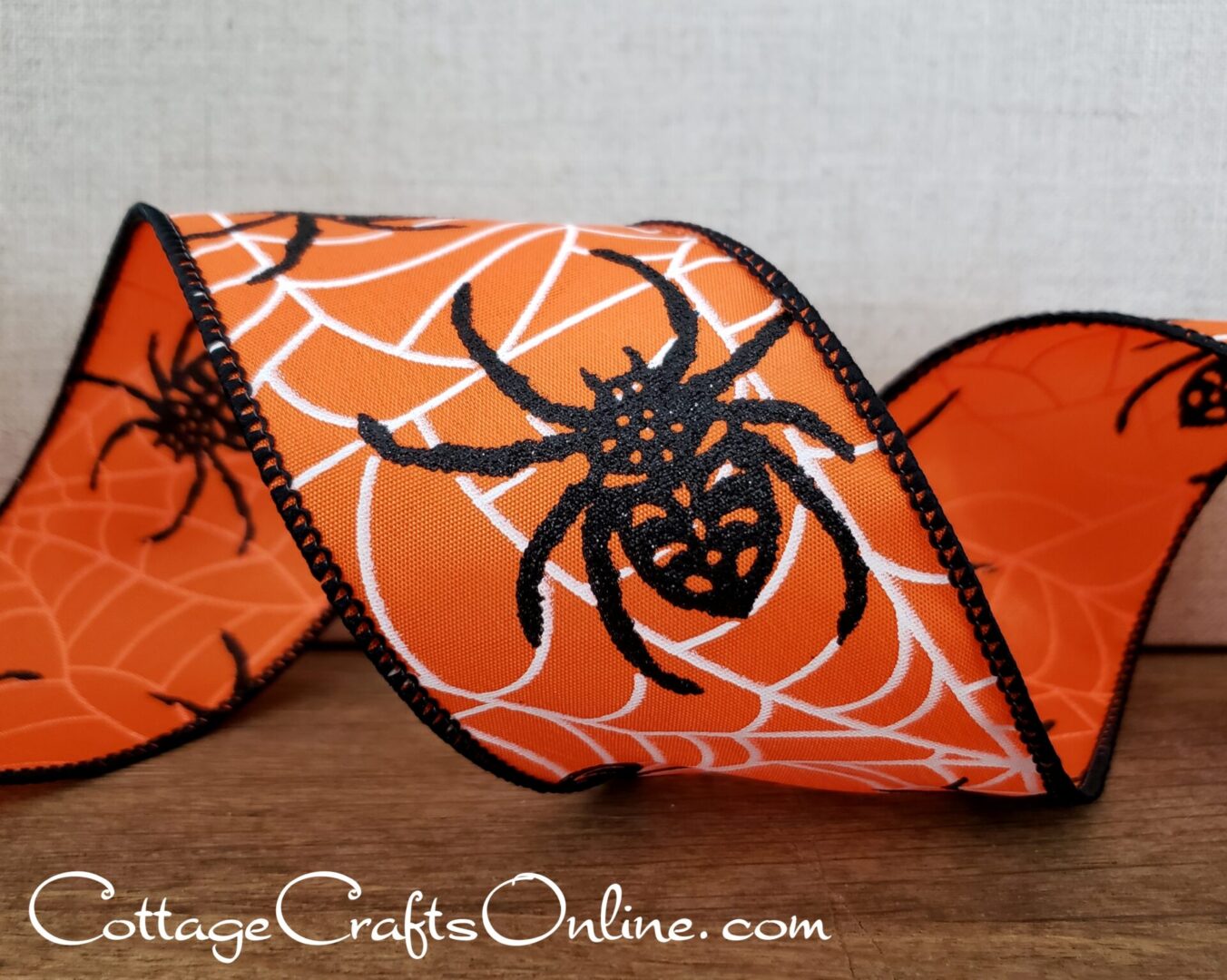 Black glitter spiders in white webs on orange satin 2.5" wide wired ribbon from the Etsy shop of Cottage Crafts Online.