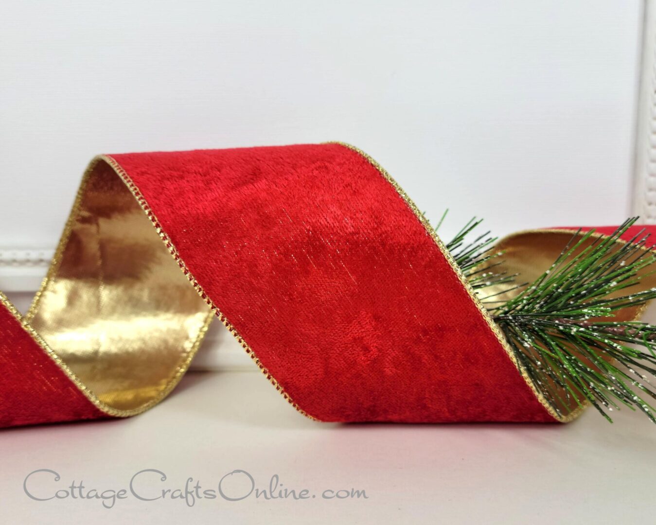 A red ribbon with gold trim and pine needles.
