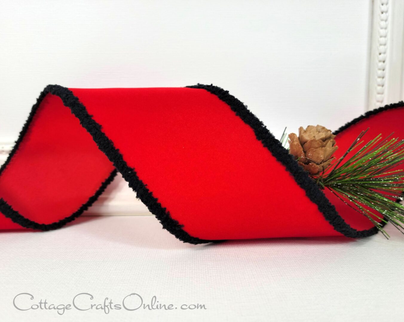 A red ribbon with black trim and pine needles.