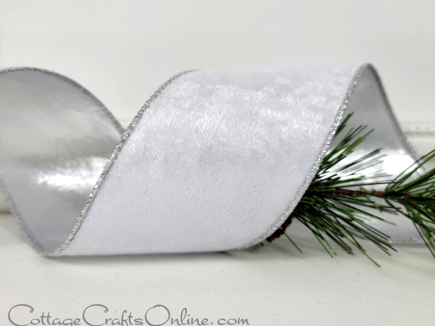 A white ribbon with silver trim and pine needles.