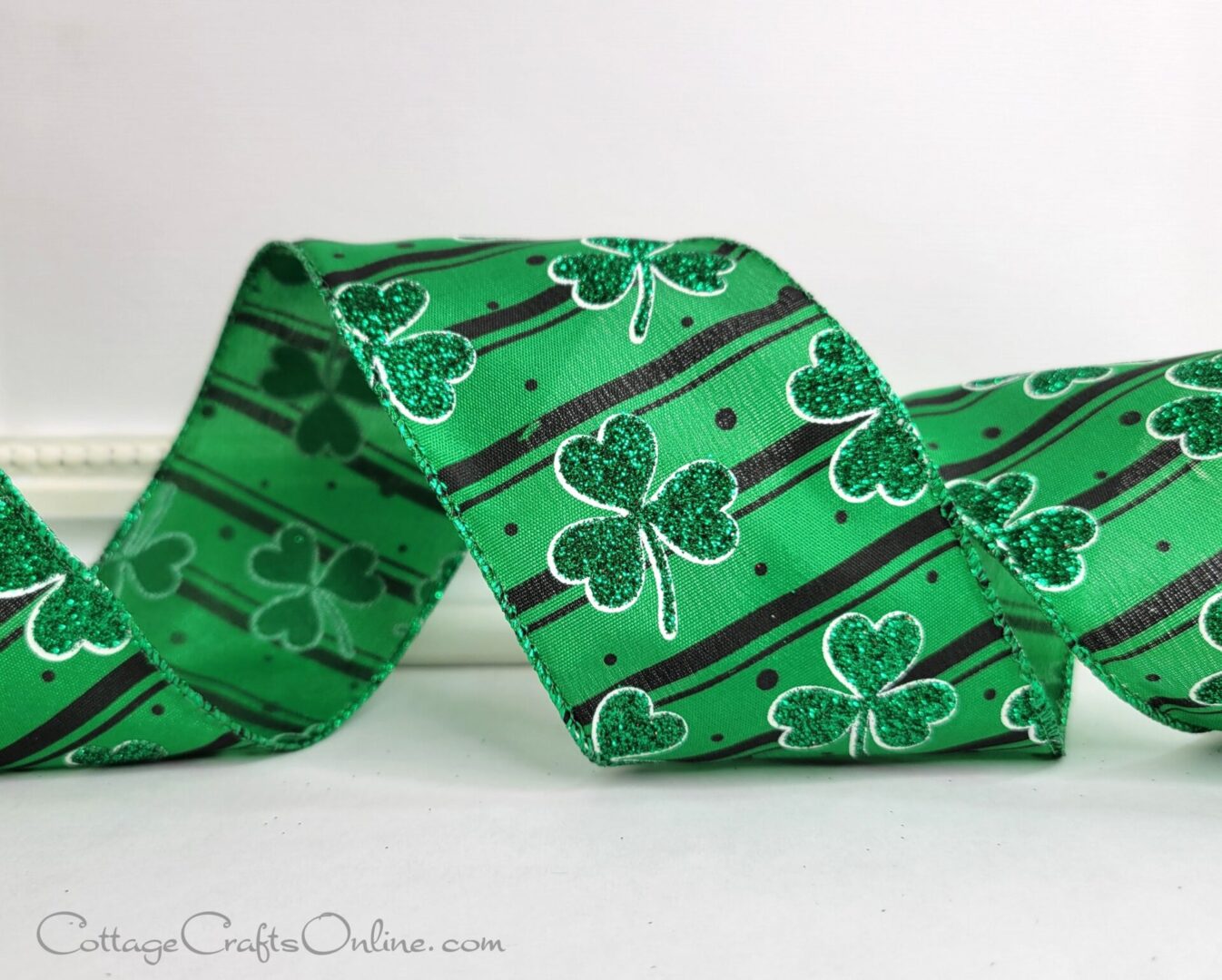 A wired edge craft ribbon showing three leafed clovers over black stripes on a green background