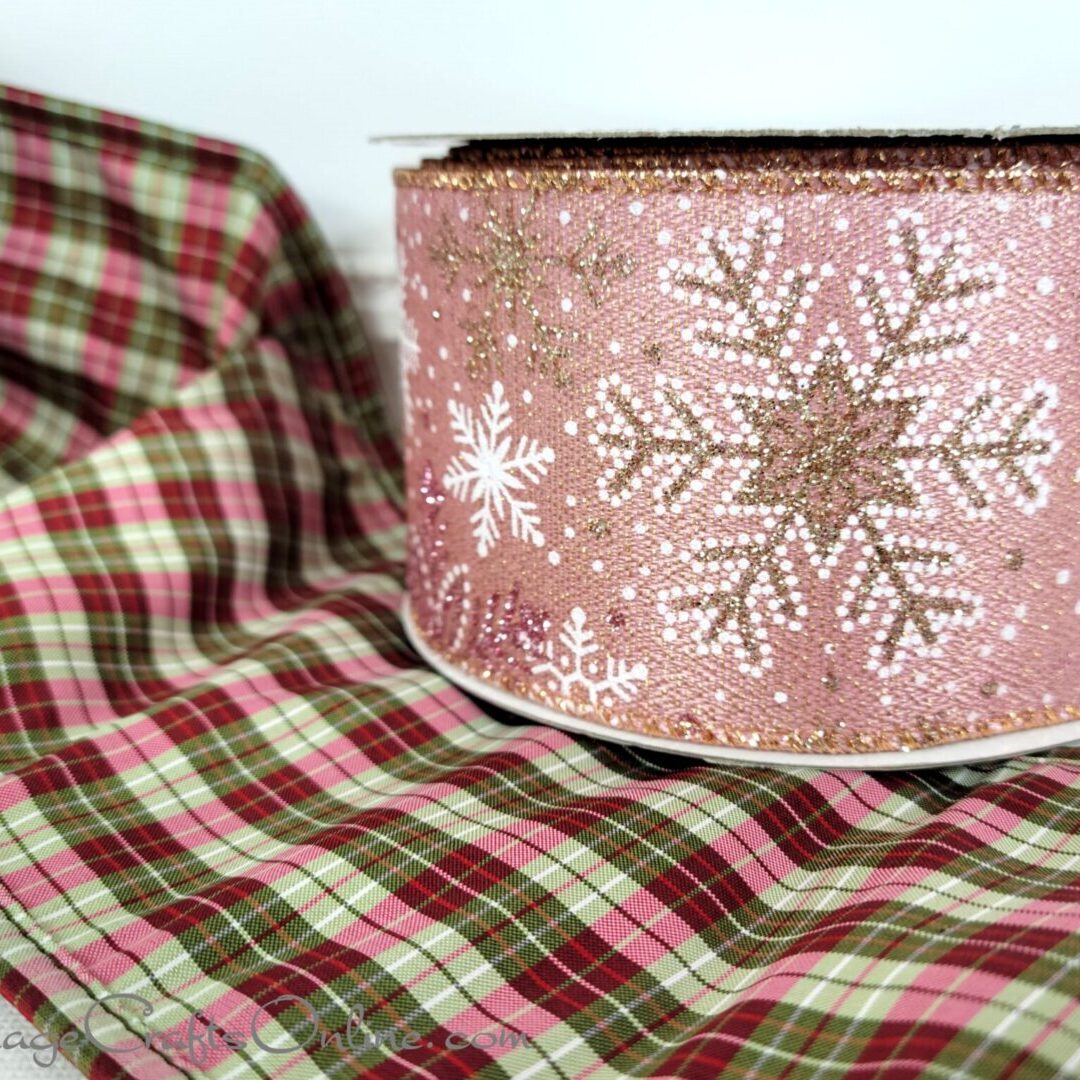 A pink and white christmas gift box on top of a plaid blanket.